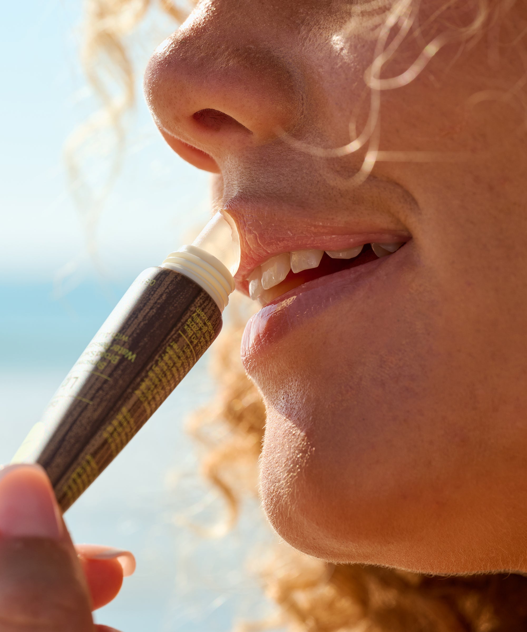 Close-up of a person applying Sun Bum Clear SPF 30 Moisturizing Lip Balm to their lips outdoors on a sunny day