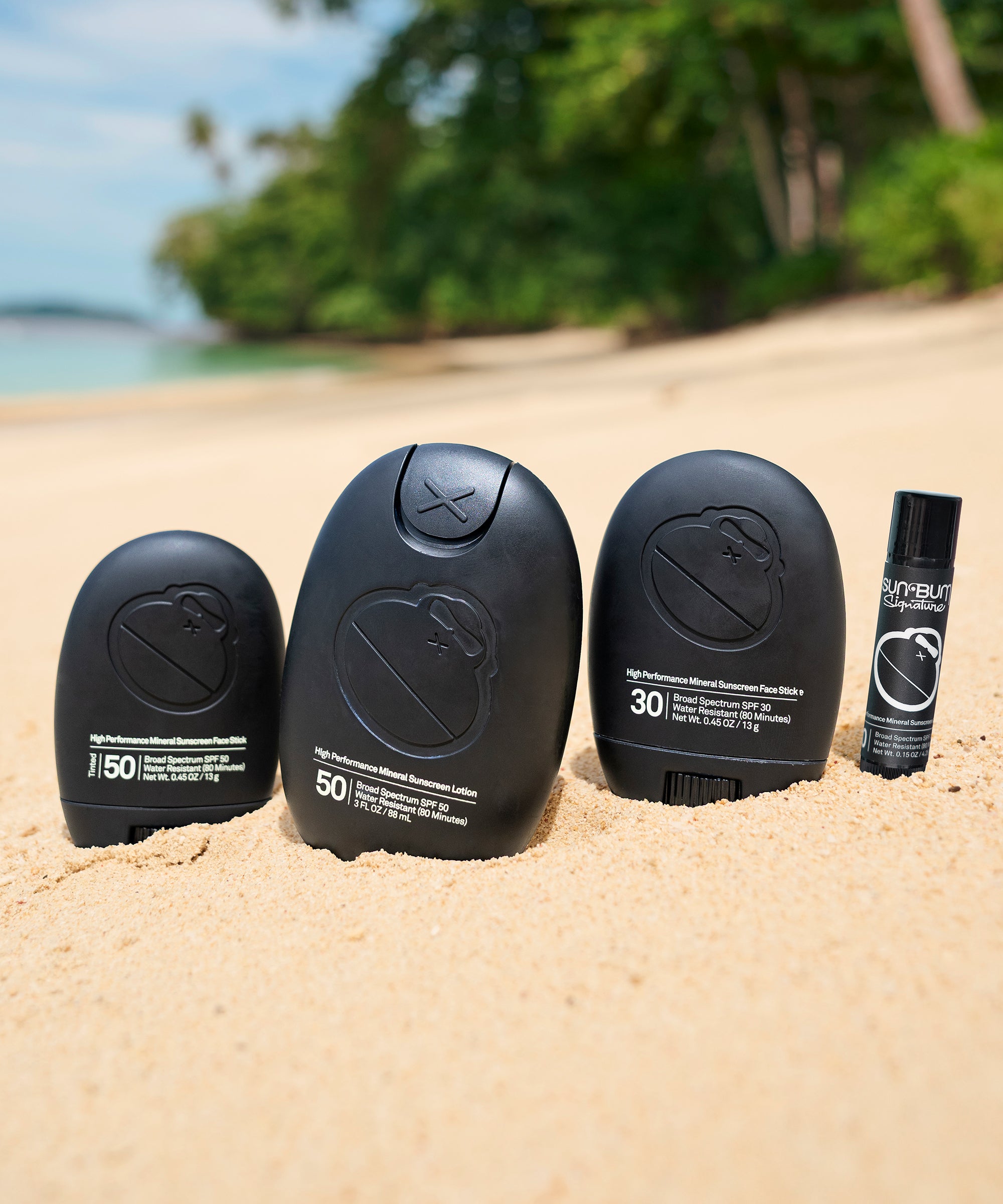 Sun Bum Signature SPF 50 Mineral Lotion and other sunscreens displayed on sandy beach with tropical background