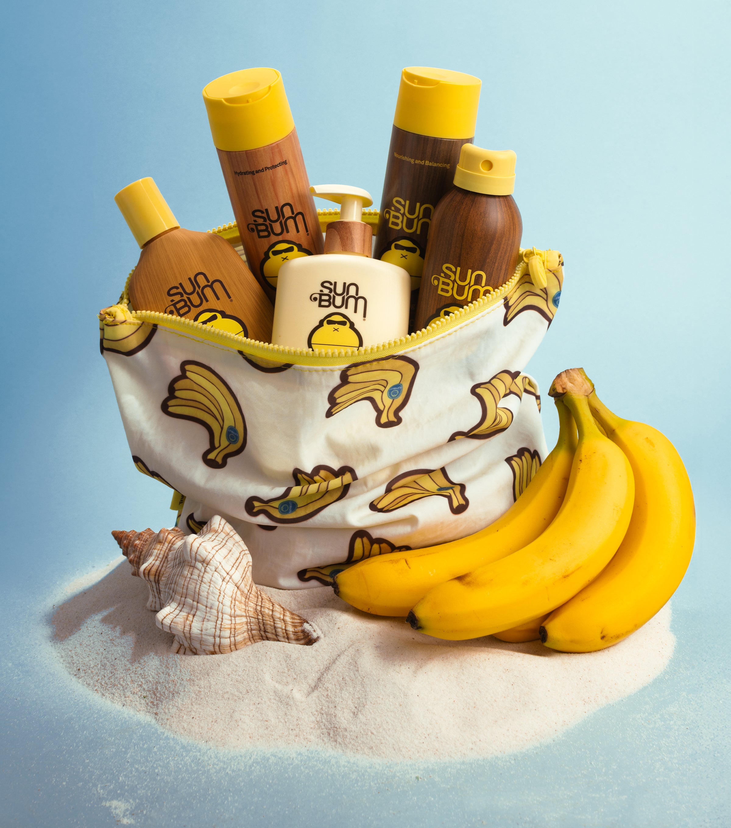Sunscreen bottles in a bag with bananas and a shell on a sandy surface