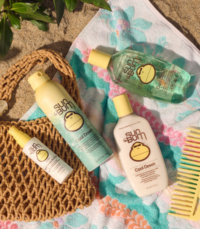 Sun Bum sunscreen bottles and a comb on a beach towel with a woven bag.