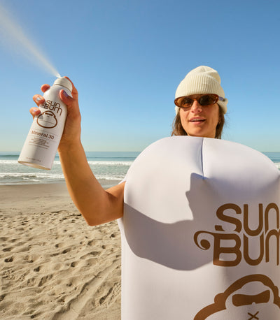 Person on a beach holding a Sun Bum sunscreen spray bottle