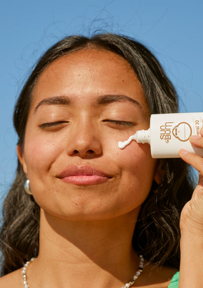 Woman applying sunscreen to her face with a clear blue sky background