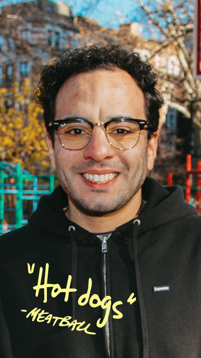 Man wearing glasses and a black hoodie with yellow text in an urban setting