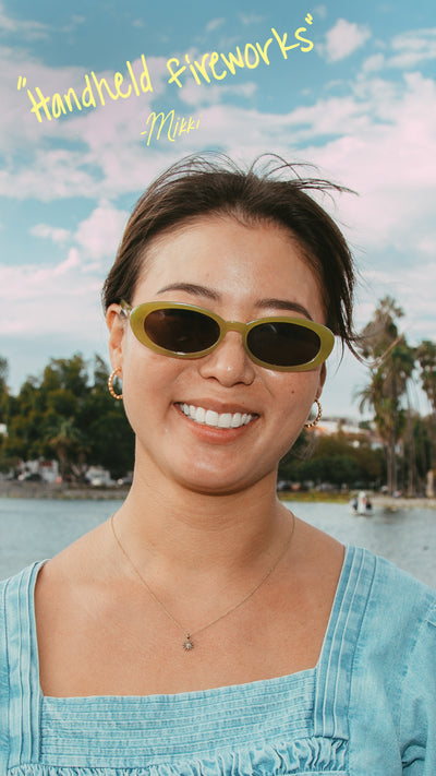 Woman wearing sunglasses with a scenic background of trees and water.