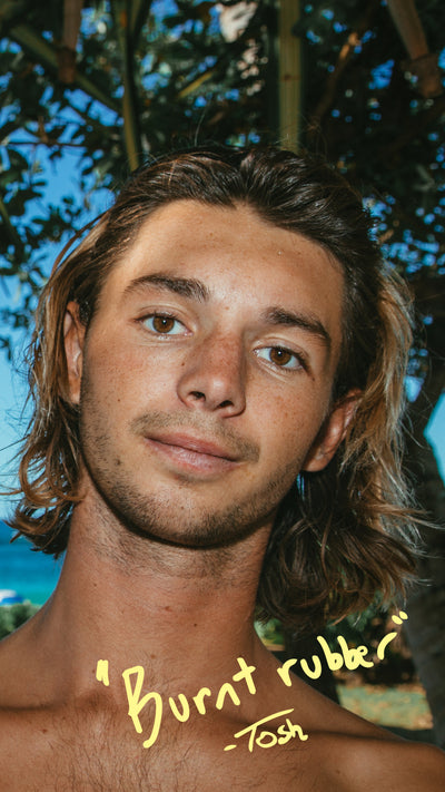 Man with long hair and a tattoo on his neck, standing outdoors with trees in the background.