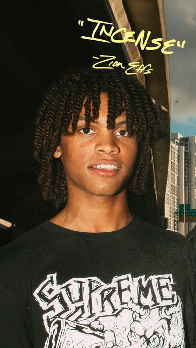 Person wearing a black Supreme t-shirt with quote that says "incense" and cityscape background
