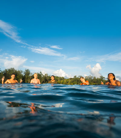 People swimming in a body of water with a clear blue sky and green trees in the background.