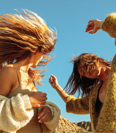 Two women dancing outdoors with textured, wind-blown hair under the sun, featuring the SB Texturizing Hair Care Collection – Sun Bum.
